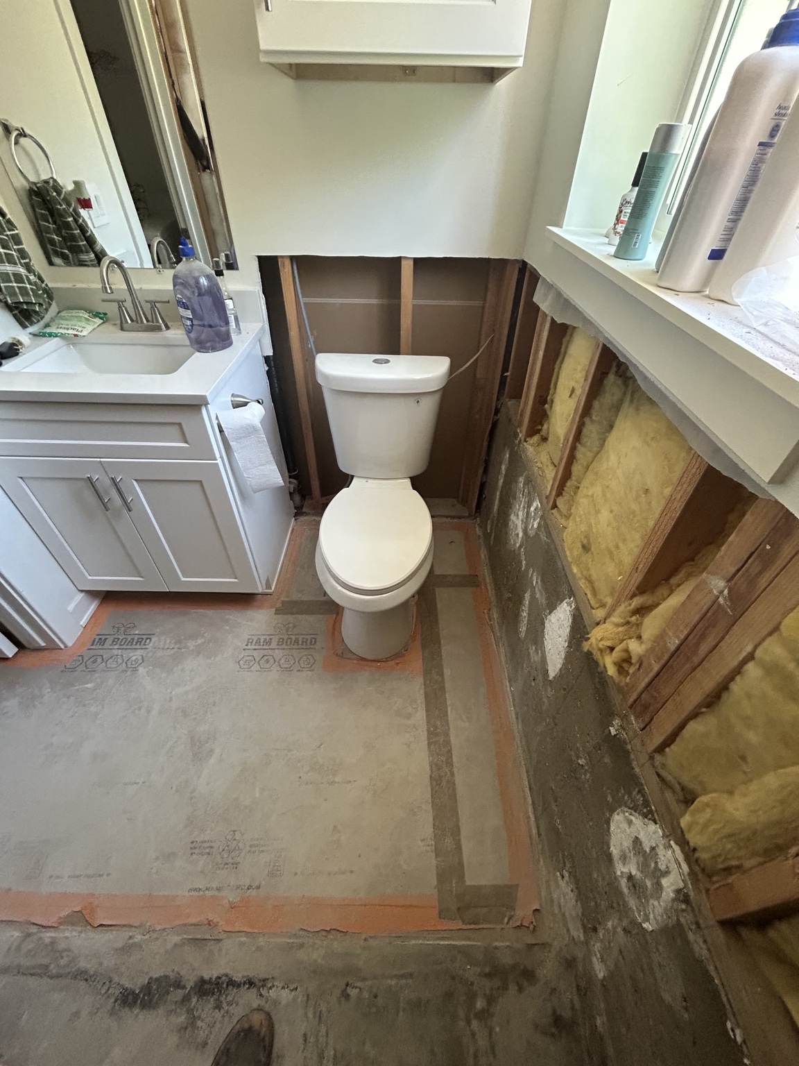 Bathroom after tile wainscoting removal, with exposed framing and protective floor covering